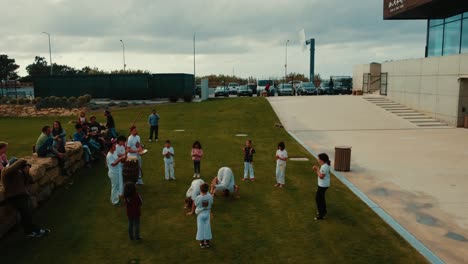 Gruppe-Von-Kindern-Spielen-Capoeira,-Brasilianische-Kampfkunst-Tanzen-Im-Grünen-Hof-Neben-Dem-Meer,-Ericeira,-Portugal