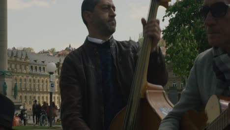 Three-street-musicians-collecting-money-and-playing-instruments-in-downtown-Stuttgart-square-at-noon,-Germany,-Europe,-panning-view-angles