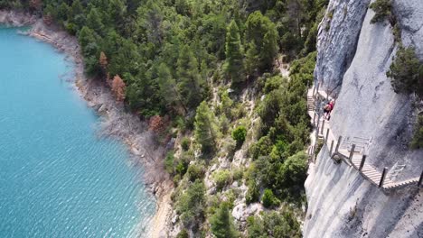 Pasarelas-de-Montfalco-Hike-at-Congost-de-Mont-Rebei-Canyon,-Catalonia-and-Aragon,-Huesca,-North-Spain---Aerial-Drone-View-of-Tourists-Walking-the-Dangerous-Scary-Stairs-along-the-Steep-Cliffs