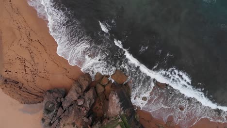 Aerial-top-down-view-of-a-rocky-beach-with-turquoise-waters-washing-it