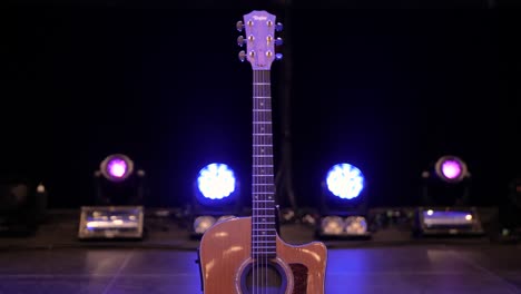 Camera-tilts-up-slowly-showing-a-Taylor-acoustic-guitar-on-a-concert-stage-with-lights