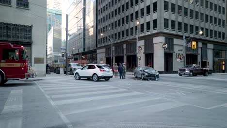 Vehicle-Collision-at-Downtown-Urban-Intersection-with-Paramedics,-Fire-Truck,-Tow-Truck-and-Pedestrians-assessing-the-Damage