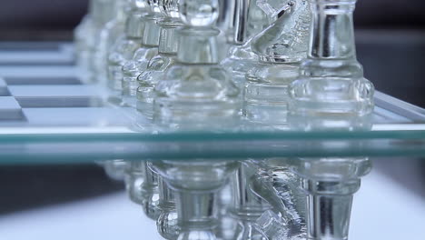 Tilt-close-shot-of-transparent-pawn-chess-pieces-inline-over-a-glassy-board-with-clear-bright-reflections-over-the-table