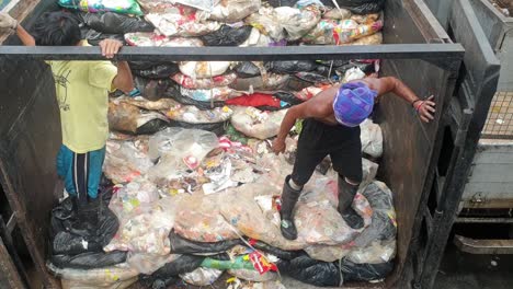 2-sanitation-workers-piling-garbage-bags-on-top-of-garbage-truck