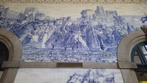 Azulejos-tile-art-inside-Sao-Bento-Train-Station-in-Porto,-Portugal-depicting-Portuguese-history,-tilt-up.