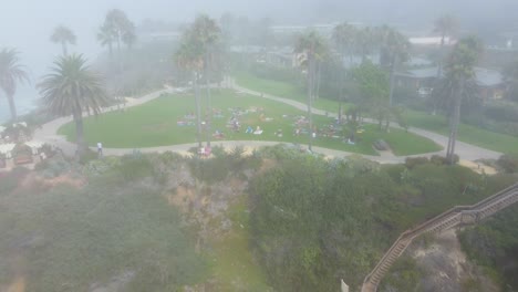 Laguna-Beach-CA-USA,-Aerial-View-of-Morning-Fog-Above-Treasure-Island-Park-and-Group-of-People-Having-Workout,-Drone-Shot