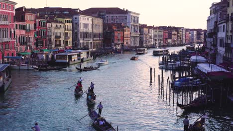 Venice---View-from-the-Rialto-Bridge-at-sunset-with-gondolas,-gondoliers,-tourists,-and-water-taxis-on-the-canals