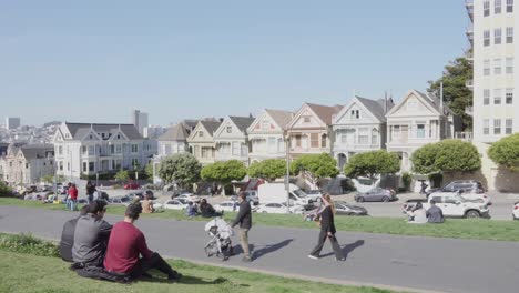 Menschen-Sitzen-Auf-Dem-Grünen-Rasen-Des-Alamo-Square-Und-Betrachten-Das-Wahrzeichen-Der-Painted-Ladies-An-Einem-Klaren,-Sonnigen-Tag-In-San-Francisco