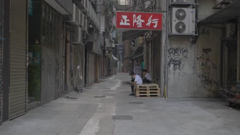 Young-from-Hong-Kong-are-taking-a-break-in-a-small-street-in-the-city-during-the-day-under-a-sign