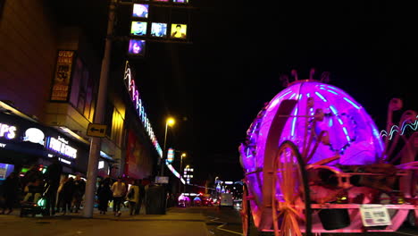 Letrero-De-Neón-De-Nhs-En-Blackpool,-Tomado-La-Noche-Del-Encendido-De-Las-Iluminaciones-En-2020-Con-Paseos-En-Carruajes-Y-Caballos-De-Neón-En-La-Carretera-Con-Tráfico