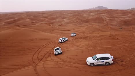 Siguiendo-Vehículos-4x4-En-Un-Desierto-De-Arena-Roja-Para-Un-Safari-Por-El-Desierto