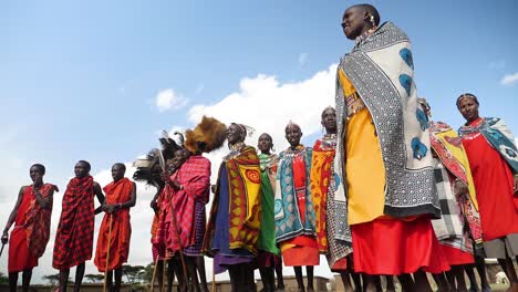 Massai-Stammesfrauen-Tanzen-Aus-Niedriger-Perspektive,-Frauen-In-Traditioneller-Kleidung-Und-Singen-Mit-Himmel-Im-Hintergrund-In-Kenia,-Masai-Mara-Nationalpark,-Zeitlupe