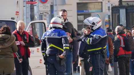 Two-police-officers-with-a-helmet-and-in-uniform-discuss-the-demonstration-itinerary-with-an-union-worker-before-the-yellow-jacket-demonstration,-another-union-worker-puts-stickers-of-his-union