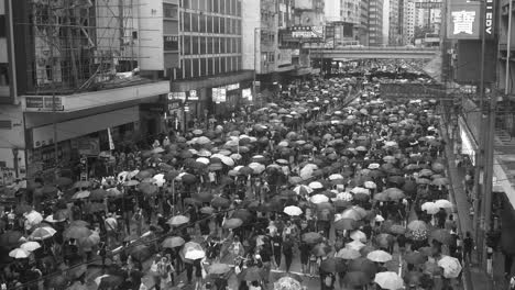 Schwarz-Weiß-Weitwinkelaufnahme-Von-Demonstranten-In-Hongkong,-Die-Im-Regen-Marschieren