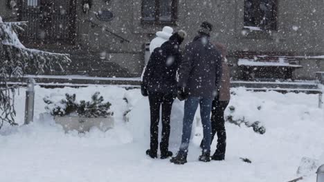 Slow-motion-shot-of-snow-fall-while-a-family-builds-a-snowman-in-the-background