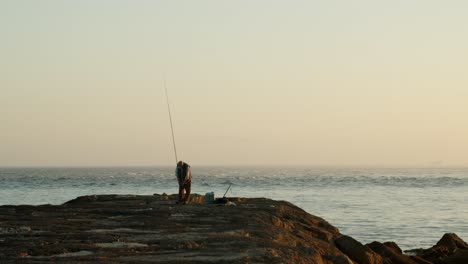 Pescador-Solitario-Preparando-Caña-De-Pescar-En-Un-Rompeolas-Al-Atardecer