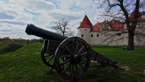 Historical-cannon-and-towers-of-Bauska-castle-in-background,-motion-view