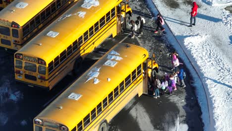 Aerial-top-down-of-kids-and-children-entering-yellow-school-bus-during-snowy-winter-day