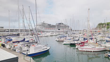 Sailboats-and-yachts-parked-near-pier-with-gigantic-cruise-ship-in-background