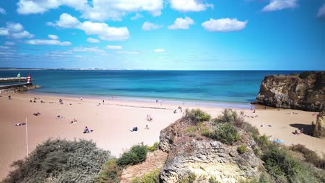 Timelapse-of-Praia-da-Batata-beach-in-Lagos,-Portugal-with-people-relaxing-under-a-bright-blue-sky