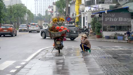 Street-Vendor,-flower-sales,-passing-vehicle-traffic,-busy-city-road