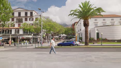 People-walk-on-sidewalk-with-scenic-Funchal-city-architecture,-Madeira