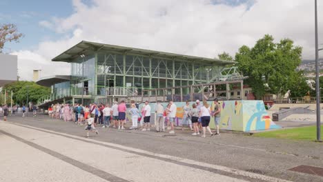 People-stand-in-long-queue-to-cable-car-station-building-Funchal-city,-Madeira