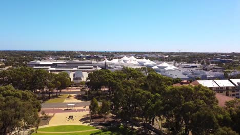 Elevación-Aérea-Sobre-Central-Park,-Joondalup-Con-El-Centro-Comercial-Junto-Al-Lago-Al-Fondo