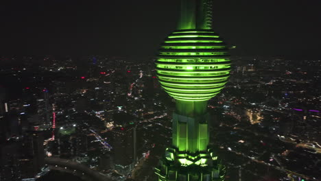 Drone-circling-the-illuminated-Petronas-Tower,-overlooking-the-cityscape-of-Kuala-Lumpur