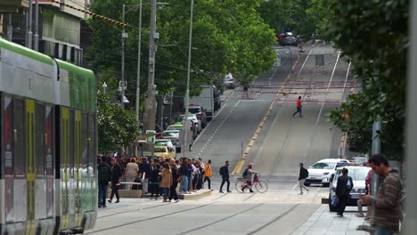 Tram-running-along-Bourke-street,-passing-through-a-bustling-city-with-pedestrians,-cyclists,-and-cars-navigating-the-urban-environment,-slow-motion-shot