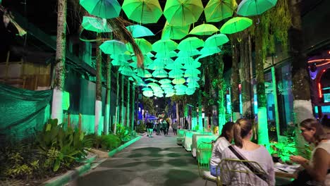 Pov-walking-under-colorful-umbrellas-on-a-bustling-street-with-bars-at-nighttime,-Medellin,-Colombia