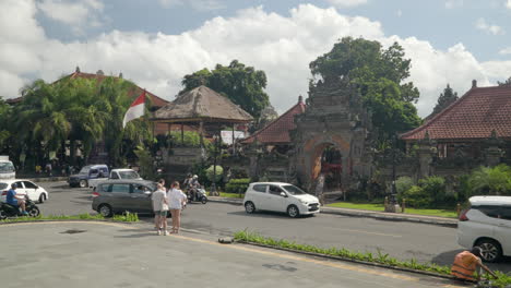 Turistas-Esperando-Cruzar-La-Concurrida-Calle-Del-Centro-De-Ubud-Hasta-La-Entrada-Del-Palacio-De-Ubud,-Bali---Cámara-Lenta,-Toma-Amplia