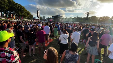 A-large-crowd-of-people-dance-in-a-field-to-music-played-by-a-band-on-a-sunny-afternoon-in-Synthony-on-the-Domain-in-Auckland,-New-Zealand