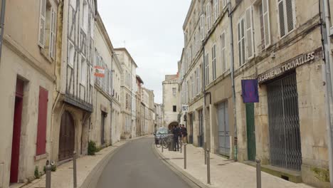 Shot-of-locals-walking-along-the-pathway-in-the-historic-center-of-La-Rochelle-district,-France-on-a-cloudy-day