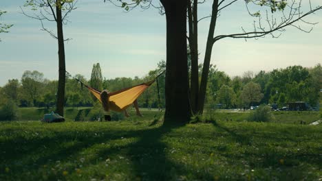 Person-relaxing-in-a-yellow-hammock-between-trees-at-Jarun-Lake,-Zagreb,-surrounded-by-lush-greenery