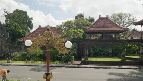 Looking-across-street-at-ancient-historical-ornate-buildings,-entry-arch-of-Ubud-Palace,-Bali---pan-left-slow-motion