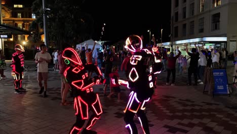 People-wearing-futuristic-light-suits-dance-in-the-Te-Komititanga-Plaza-on-Queens-Street-in-New-Zealand-at-night