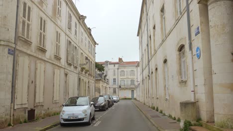 Pan-shot-of-empty-road-with-parked-cars-in-the-historic-town-of-La-Rochelle,-France-on-a-cloudy-day