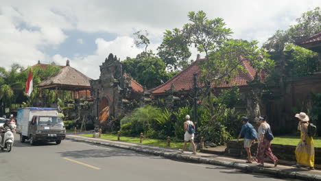 Ubud-Palace-visitors-stroll-along-sidewalk-while-traffic-passes-by,-slow-motion