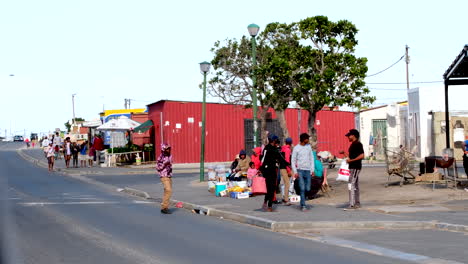 Township-residents-walk-on-pavement-past-hawkers-selling-products,-Zwelihle