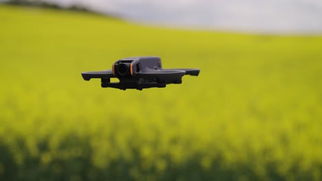 FPV-drone-with-propeller-guards-hover-in-air-near-rapeseed-field,-Czechia