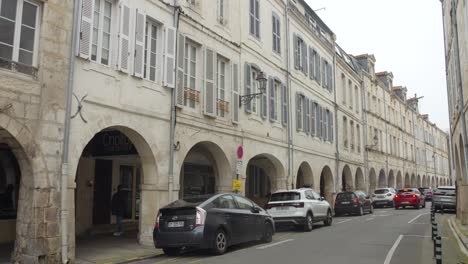 People-walking-and-cars-parked-in-the-historic-center-of-La-Rochelle,-France-on-a-cloudy-day