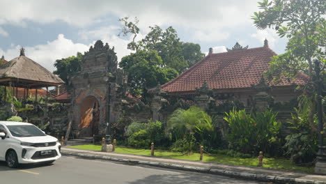 Main-entryway-to-Ubud-Palace-in-Bali,-dolly-side-walking-point-of-view-from-across-busy-street