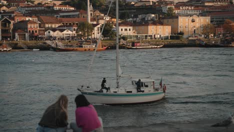 Leute-Beobachten-Segelboot-Am-Flussufer-Von-Porto,-Lebendige-Hafenszene-Bei-Sonnenuntergang