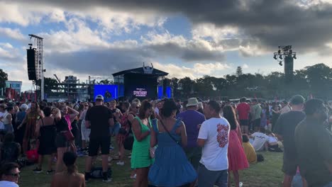 A-large-group-of-people-dance-as-they-enjoy-an-outdoor-concert-at-a-music-festival-on-a-cloudy-day-at-Synthony-on-the-Domain-in-Auckland,-New-Zealand