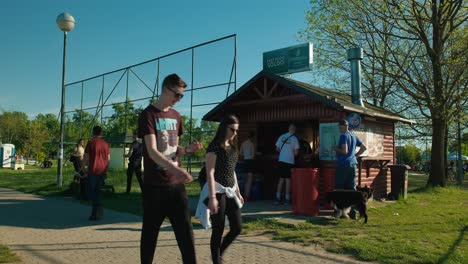 Gente-Caminando-Y-Comprando-Bocadillos-En-Un-Puesto-De-Comida-Cerca-De-Una-Cancha-De-Fútbol-En-El-Lago-Jarun-En-Zagreb,-Croacia,-En-Un-Día-Soleado