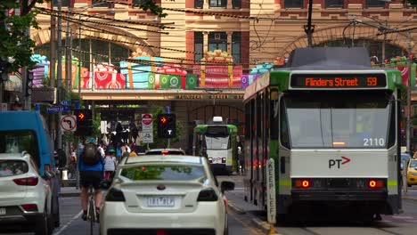 Slow-motion-shot-capturing-the-hustle-and-bustle-of-Melbourne-city,-with-vehicle-traffic,-cyclists-and-trams-running-along-Elizabeth-Street-towards-Flinders-Street-station