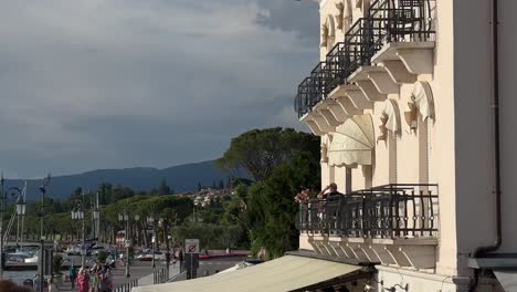 Turista-En-El-Balcón-Italiano-Del-Hotel-Disfrutando-Del-Atardecer-En-Lazise,-Lago-De-Garda