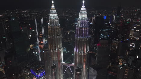 Drone-tilting-around-the-illuminated-Petronas-Twin-Towers,-night-in-KL,-Malaysia