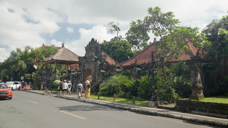 Street-traffic,-pedestrians-moving-past-entrance-to-Ubud-Palace-in-Bali